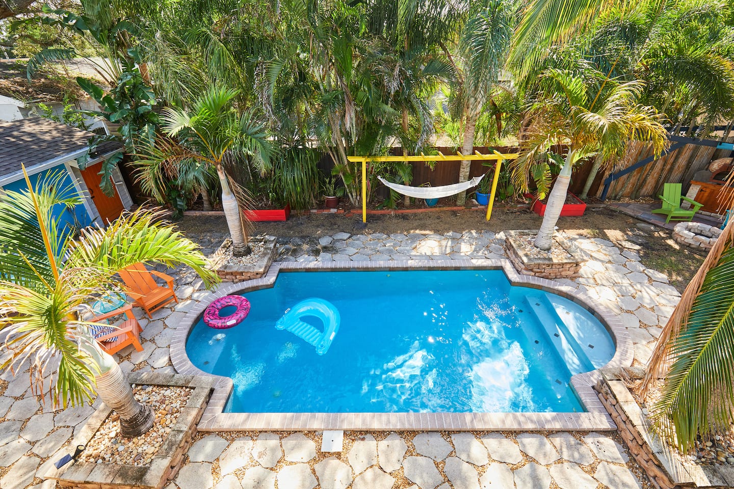 The pool from above, floats on the water, enclosed by palms and a wooden fence.