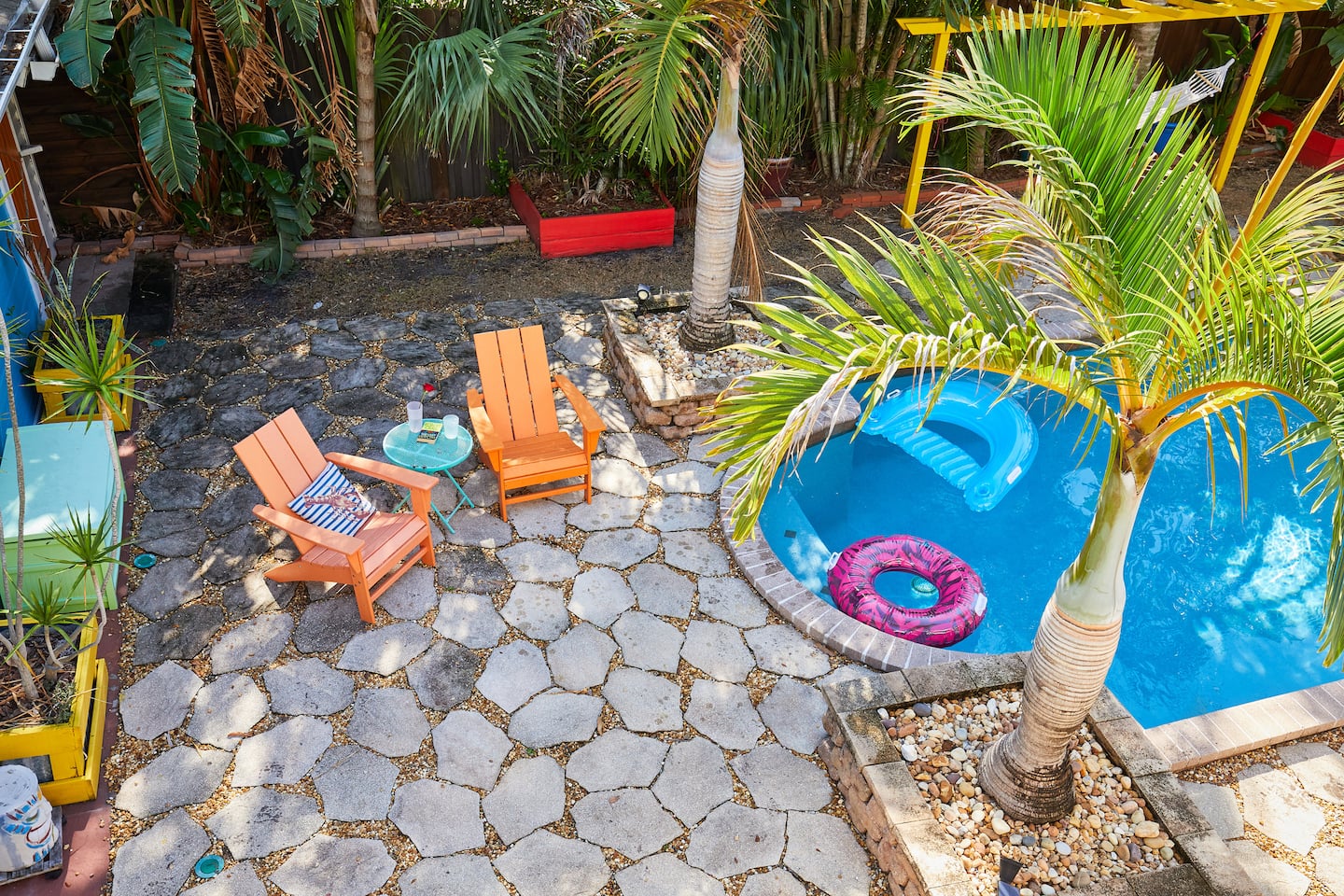 Orange Adirondack chairs and a small table on the flagstone patio at the pool's edge.
